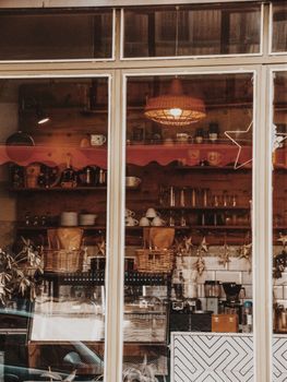 Through glass of cups and glassware with coffee maker under lamp in cafe