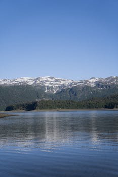 A tranquil lake with mountain reflections and snowcapped peaks under a clear blue sky.