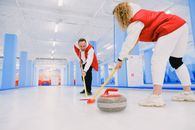 Low angle of male and female players sweeping ice sheet with brooms in path of granite stone during curling training