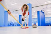 Ground level of cheerful woman and crop curler with curling brooms sweeping ice sheet in front of rock during training on rink