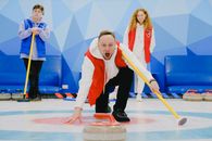 Excited sportsman with open mouth in activewear standing on knee with broom and throwing stone with red handle while playing curling on ice rink