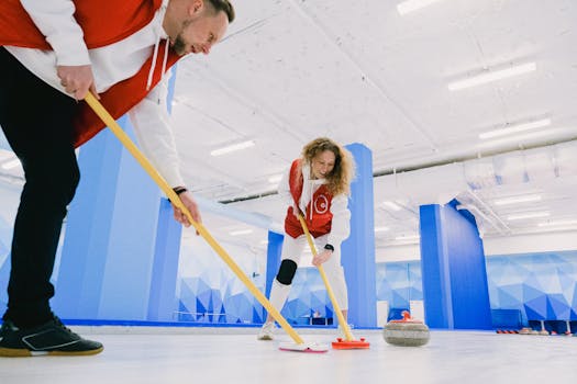 Two athletes practicing curling indoors with focus on teamwork and precision.