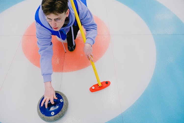 Curling Player Delivering Stone To House On Ice Rink