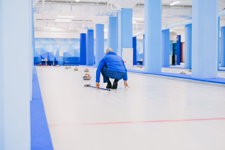 Sportsman Playing Curling On Modern Ice Rink With Blue Walls