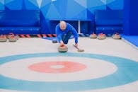 Focused male in blue activewear choosing tactic and throwing stone while playing curling on ice rink