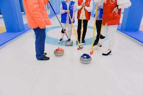 Crop players of curling professional team in sportswear with brooms and stones standing on ice rink