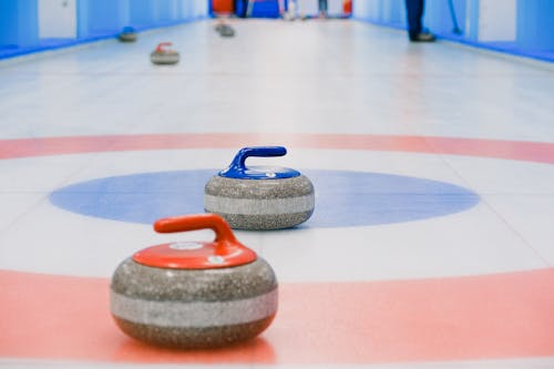 Red and blue handled curling stones placed on circles of house of ice arena while competition