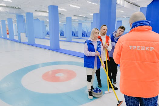 Curling team discussing strategy during practice on an indoor rink with coach.