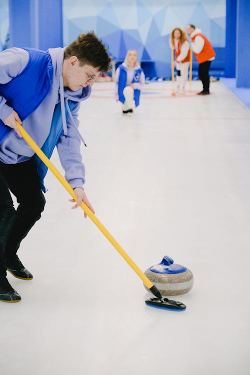 Young man sweeping ice with broom for moving stone