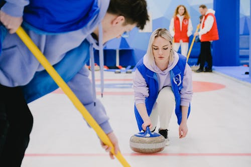 Young man sweeping ice with broom and woman moving stone