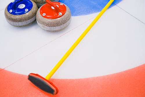 From above of granite curling stone and broom placed on ice sheet in house with colorful target area in playing area