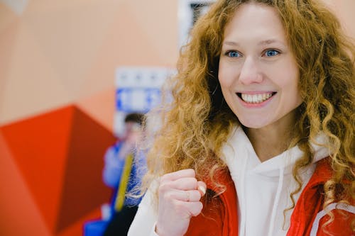 Free Gleeful sportswoman with curly hair in sportswear cheering for team with clenched fists and looking away while standing in arena during curling game Stock Photo