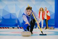 Concentrate male in sportswear with broom in hand throwing granite curling stone sliding on ice sheet while playing game near team