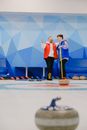 Sportsmen in warm waistcoats smiling while standing together near wall in curling arena