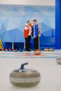 Male curler pointing with hand while standing with teammate near blue wall of sheet