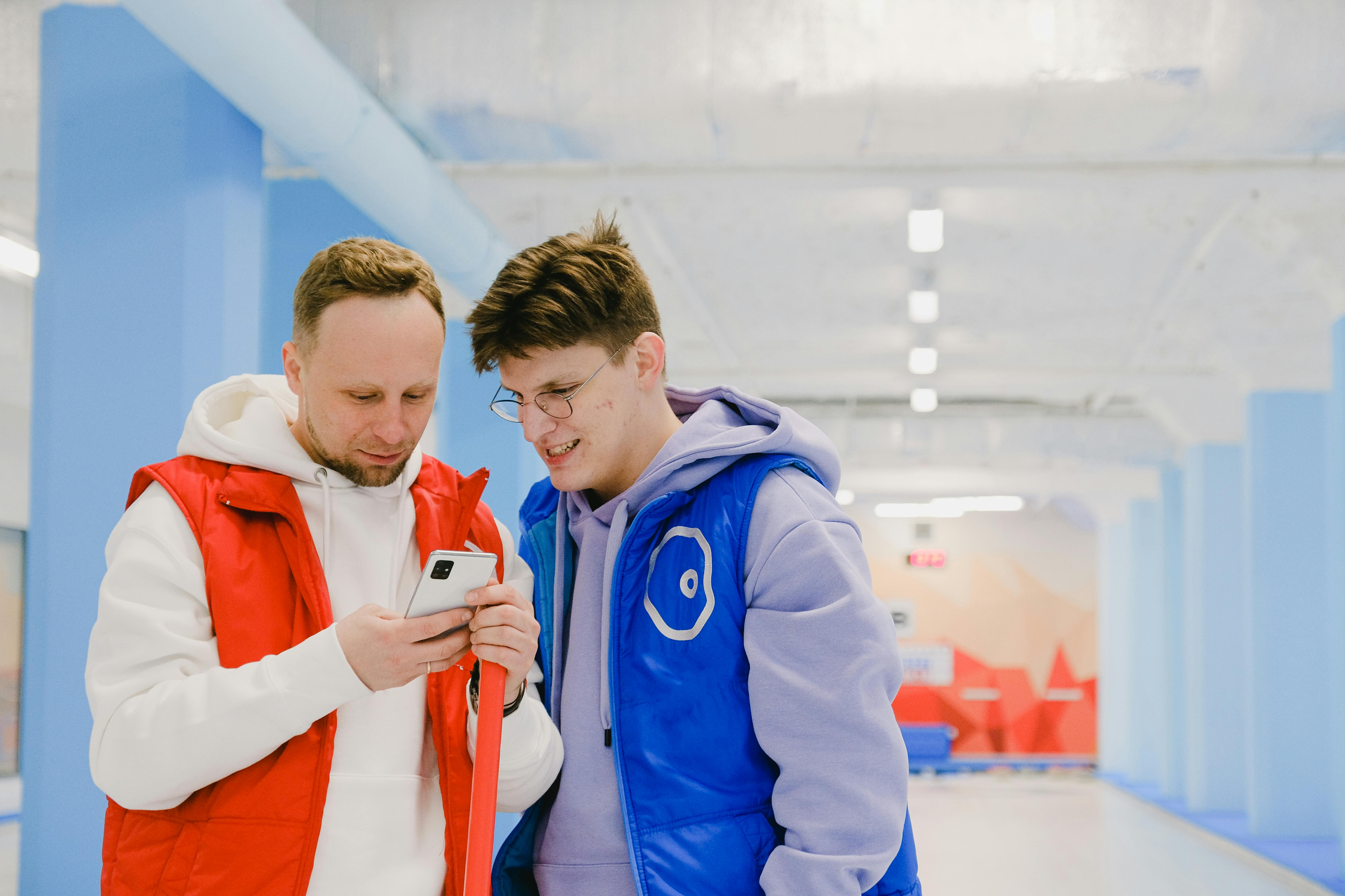 man showing smartphone screen to friend in curling court