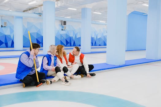 Sportsmen in red and blue waistcoats chatting on floor of spacious curling arena