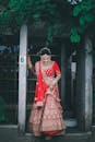 Woman in Traditional Red Wedding Dress Standing Under Green Leaves