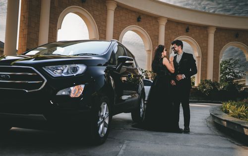 Free A stylish couple standing next to a luxurious black SUV, capturing a moment of elegance. Stock Photo