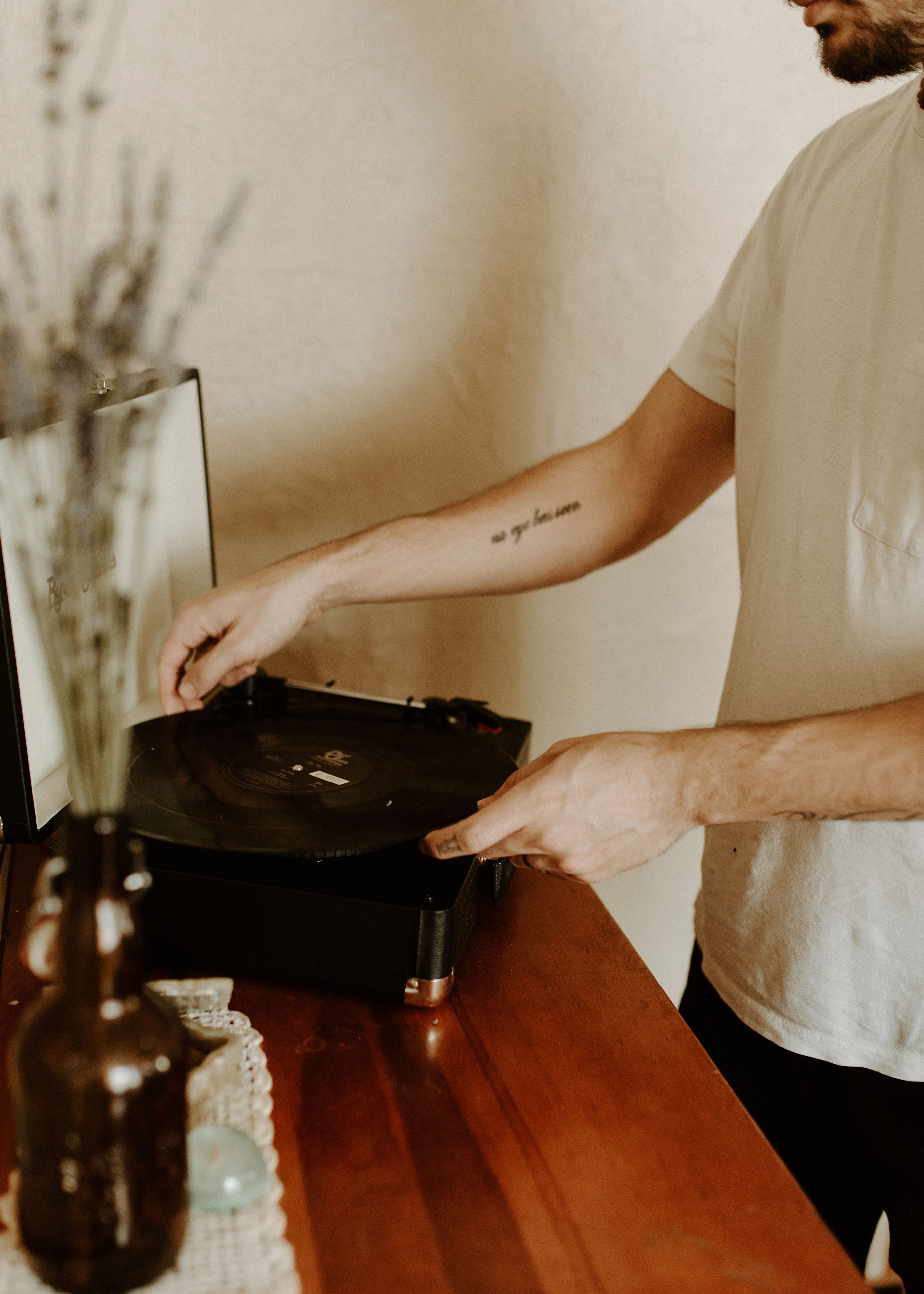 Adult man adjusting vinyl record on turntable in a cozy room, capturing a vintage vibe.