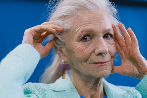 Free Elderly female model looking at camera on blue background with hands against face Stock Photo