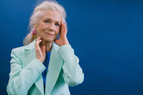Free Elegant elderly woman in trendy clothes looking at camera and touching face while standing on blue background Stock Photo
