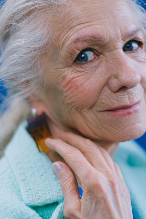 Free Blue eyed elderly woman in green outfit looking at camera while touching face Stock Photo