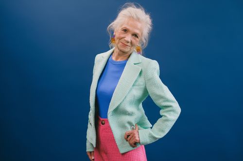Free Delightful gray haired female in stylish green suit putting hand on waist and looking at camera against blue background Stock Photo