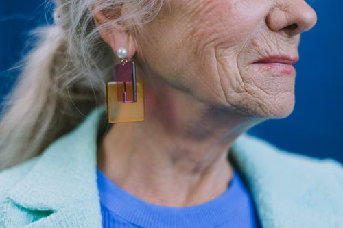 Free Crop unrecognizable old female with gray hair and creative earring looking away on blue background Stock Photo