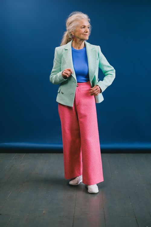 Free Full body of aged female model in stylish pants and trendy jacket looking away against blue background Stock Photo