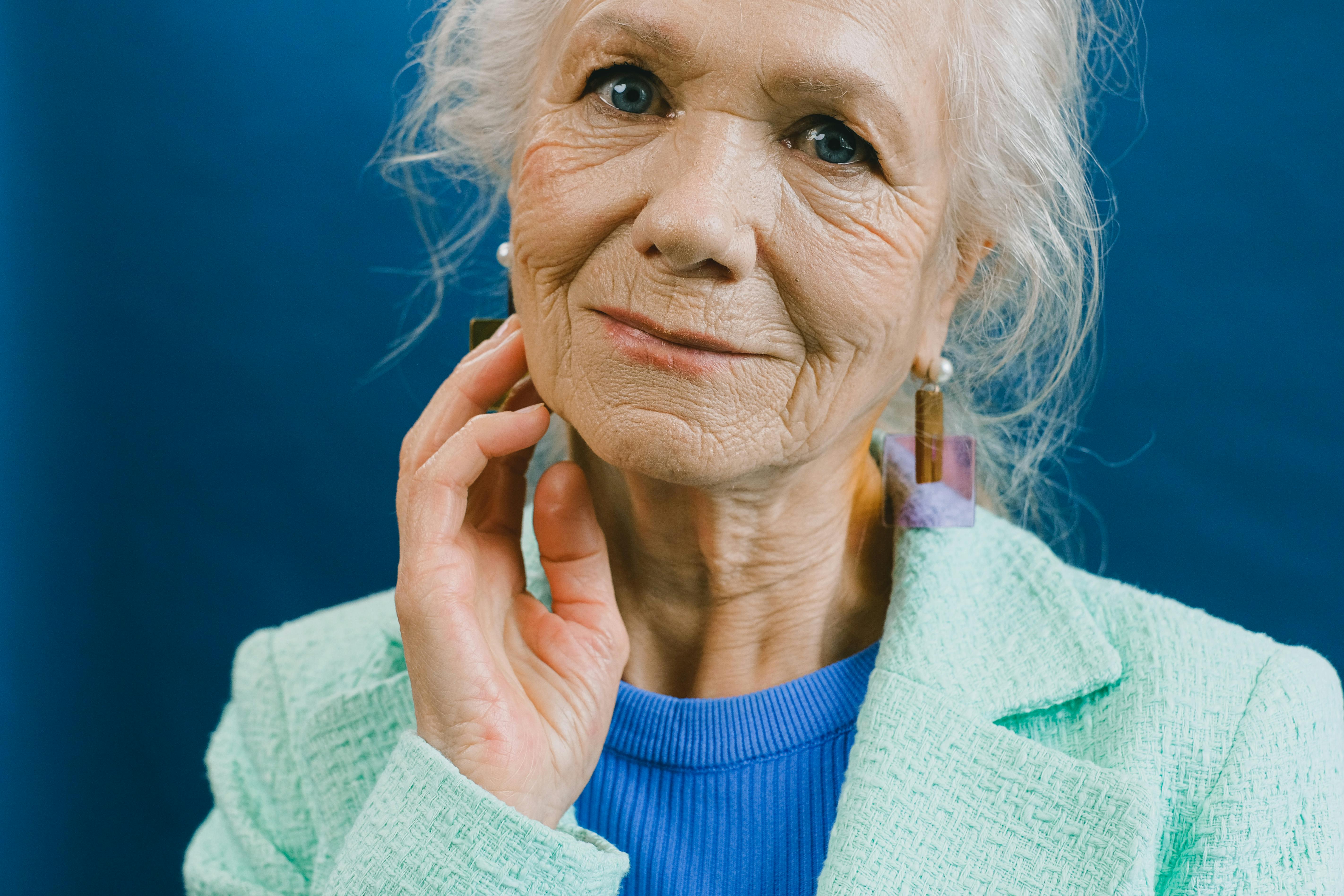 elderly lady touching face against blue backdrop