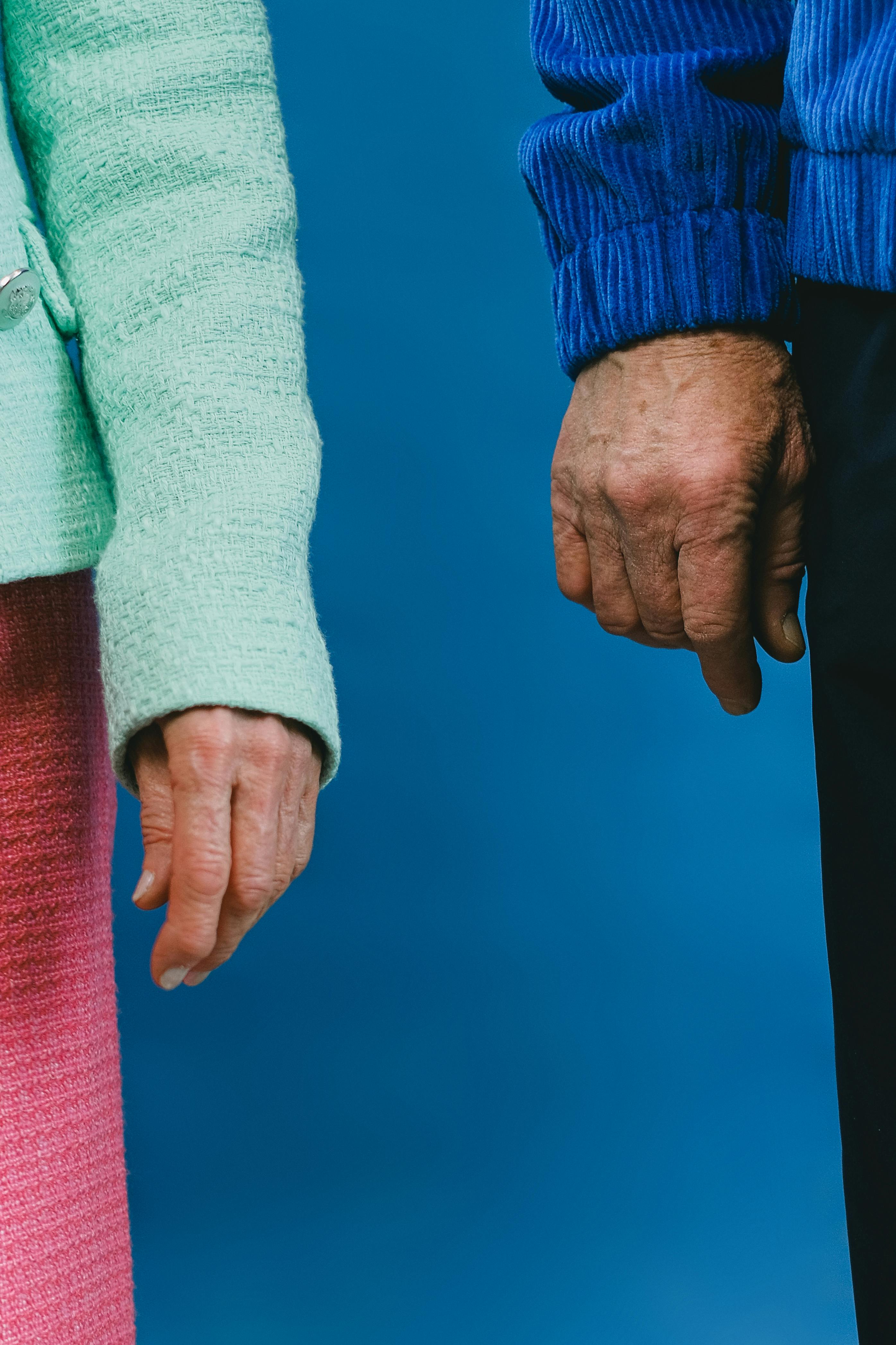 Close-up of senior couple's hands side by side against a blue backdrop, symbolizing unity and love.