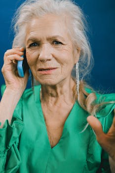 Senior woman with gray hair in a green dress having a phone conversation.