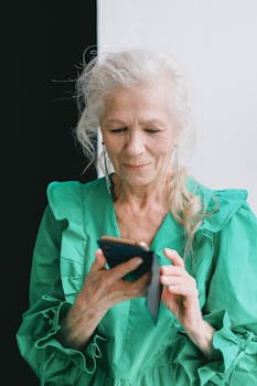 Senior woman happily using smartphone in bright green attire.