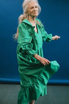 A senior woman gracefully dancing in a vibrant green dress with a blue background.