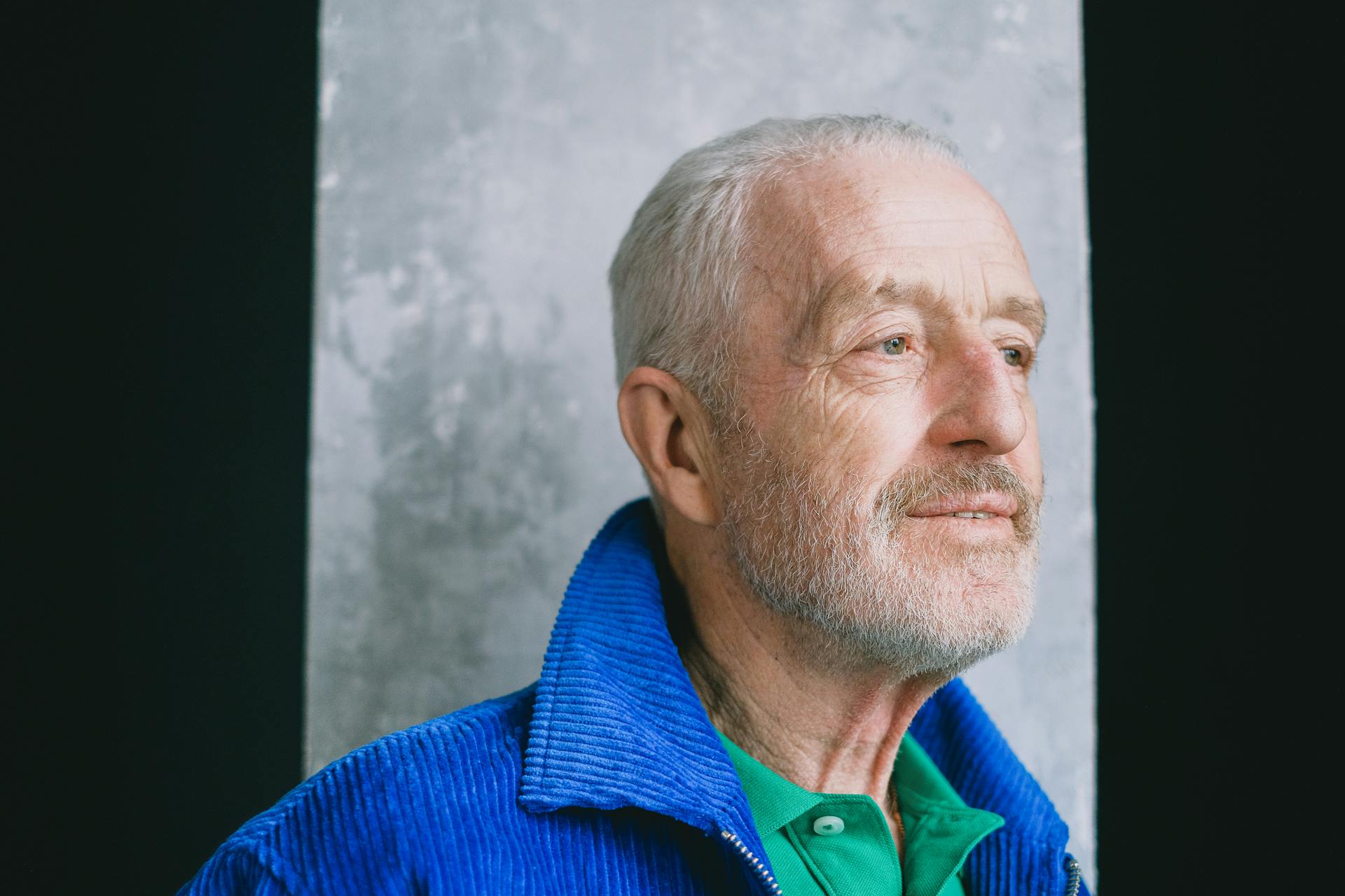 Portrait of a senior man with facial hair in a blue jacket looking away contemplatively.