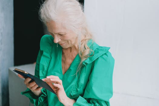 Happy senior woman in green blouse smiling at smartphone indoors.