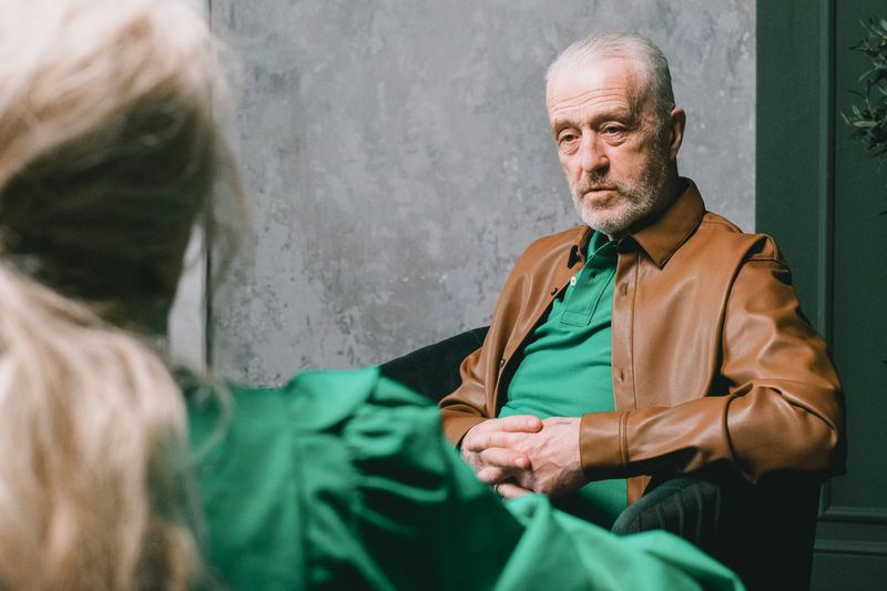 Elderly man in brown leather jacket during a conversation indoors.