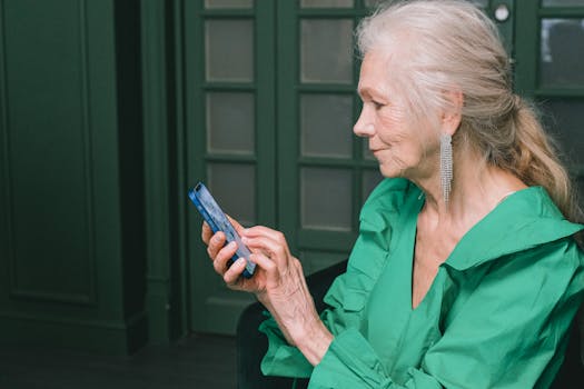Elegant senior woman in green dress using a smartphone indoors with a focused expression.
