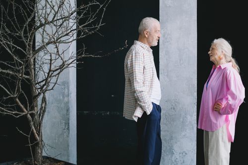 Free Elderly man and woman sharing a joyful conversation indoors next to a leafless tree. Stock Photo