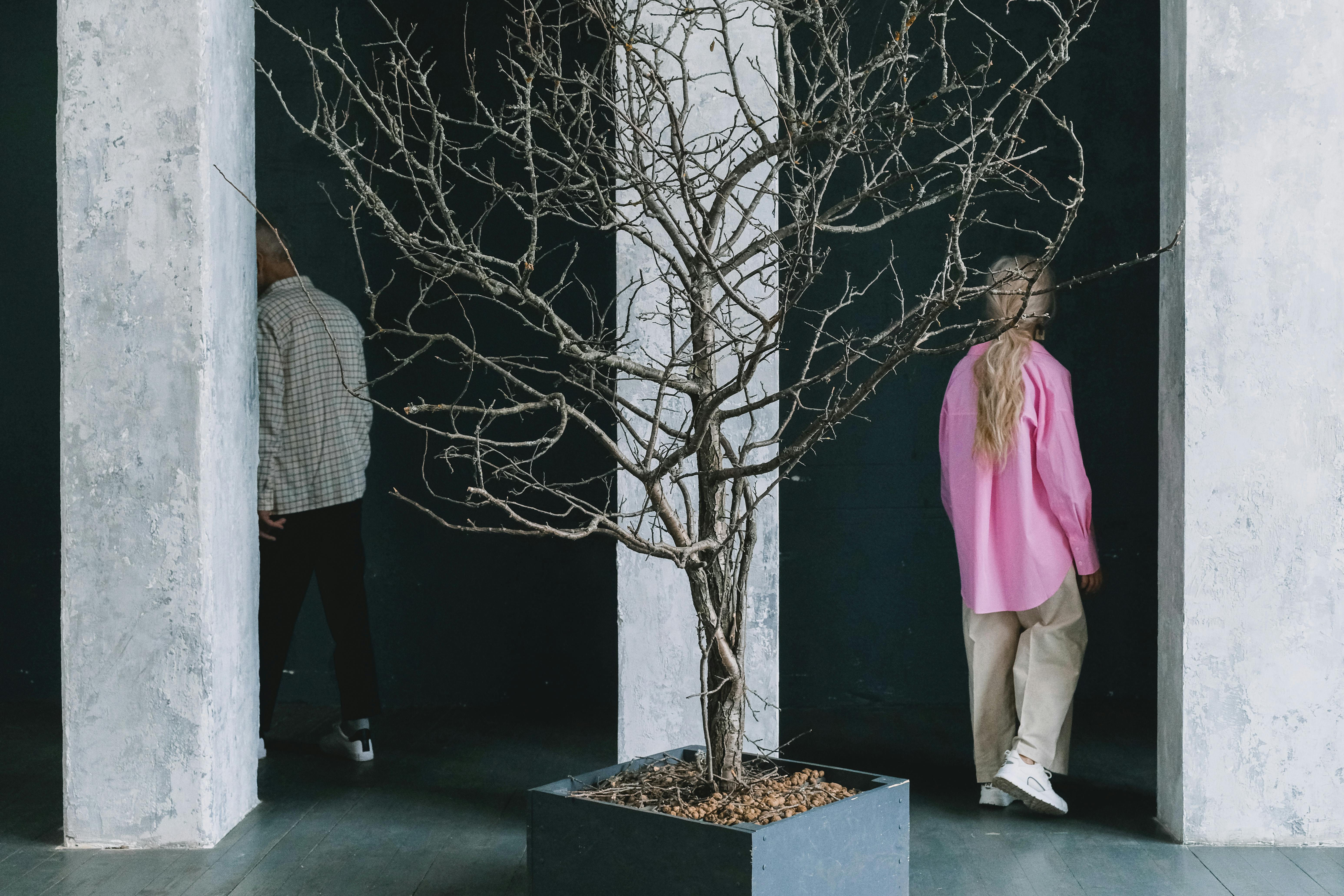A creative indoor setup featuring two people and a bare tree, emphasizing contrast and symmetry.