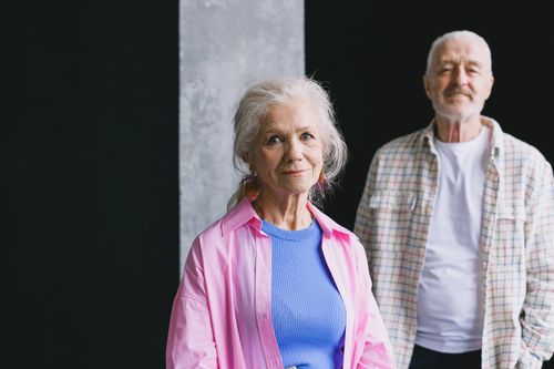Free A senior couple smiling warmly indoors, with checkered and pink shirts. Stock Photo