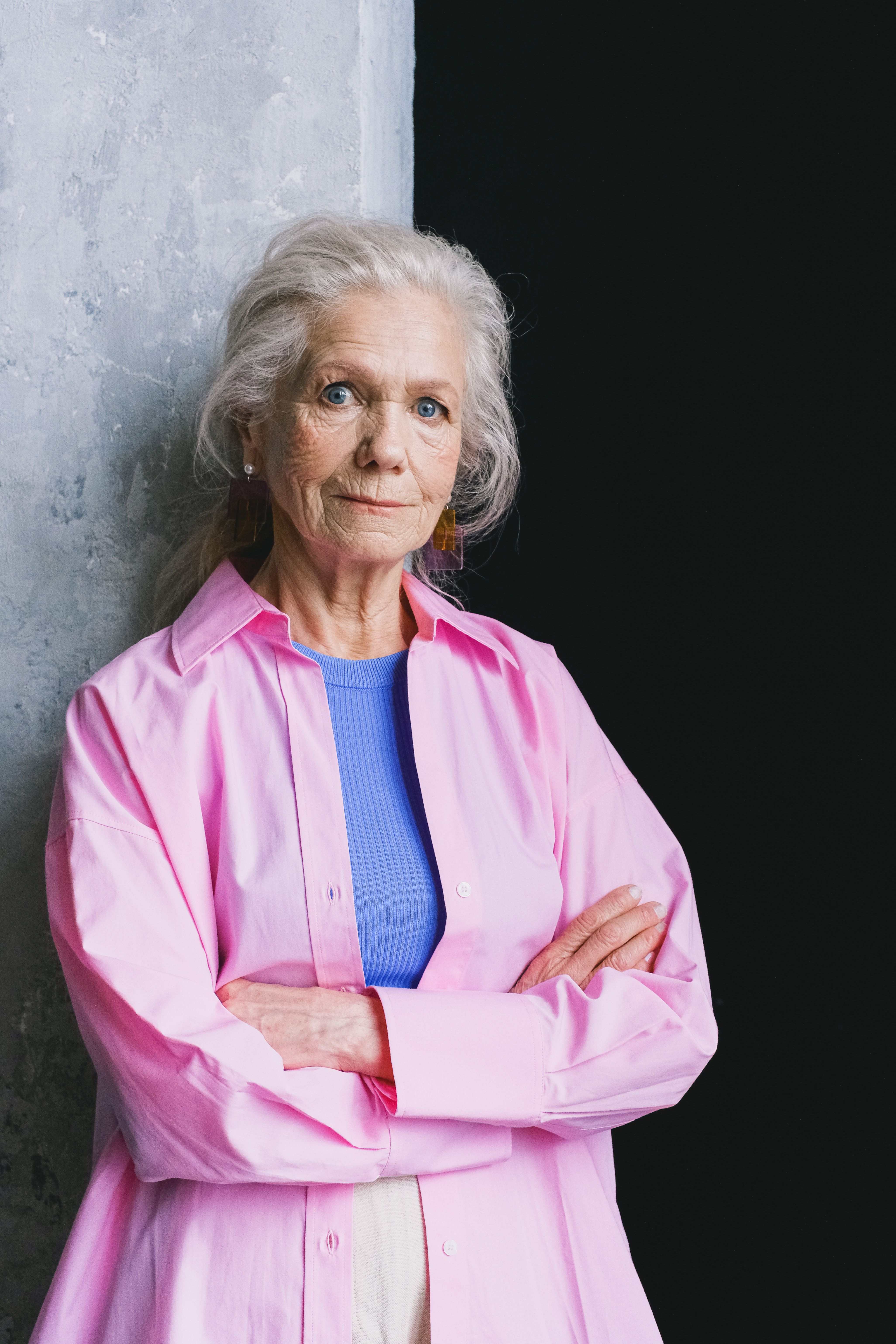 Portrait of a confident senior woman in a stylish pink shirt against a concrete wall.