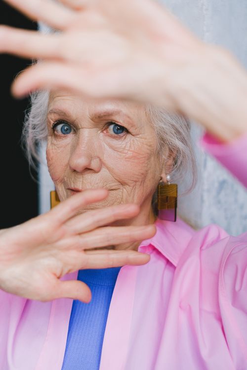 Free Close-up of a senior woman with blue eyes and vibrant clothing, emphasizing expression and style. Stock Photo
