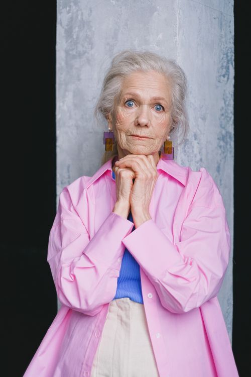Free Portrait of a senior woman with blue eyes in a pink shirt, posing with hands together. Stock Photo