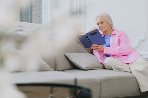 Elderly Woman Sitting on a Sofa While Reading a Book