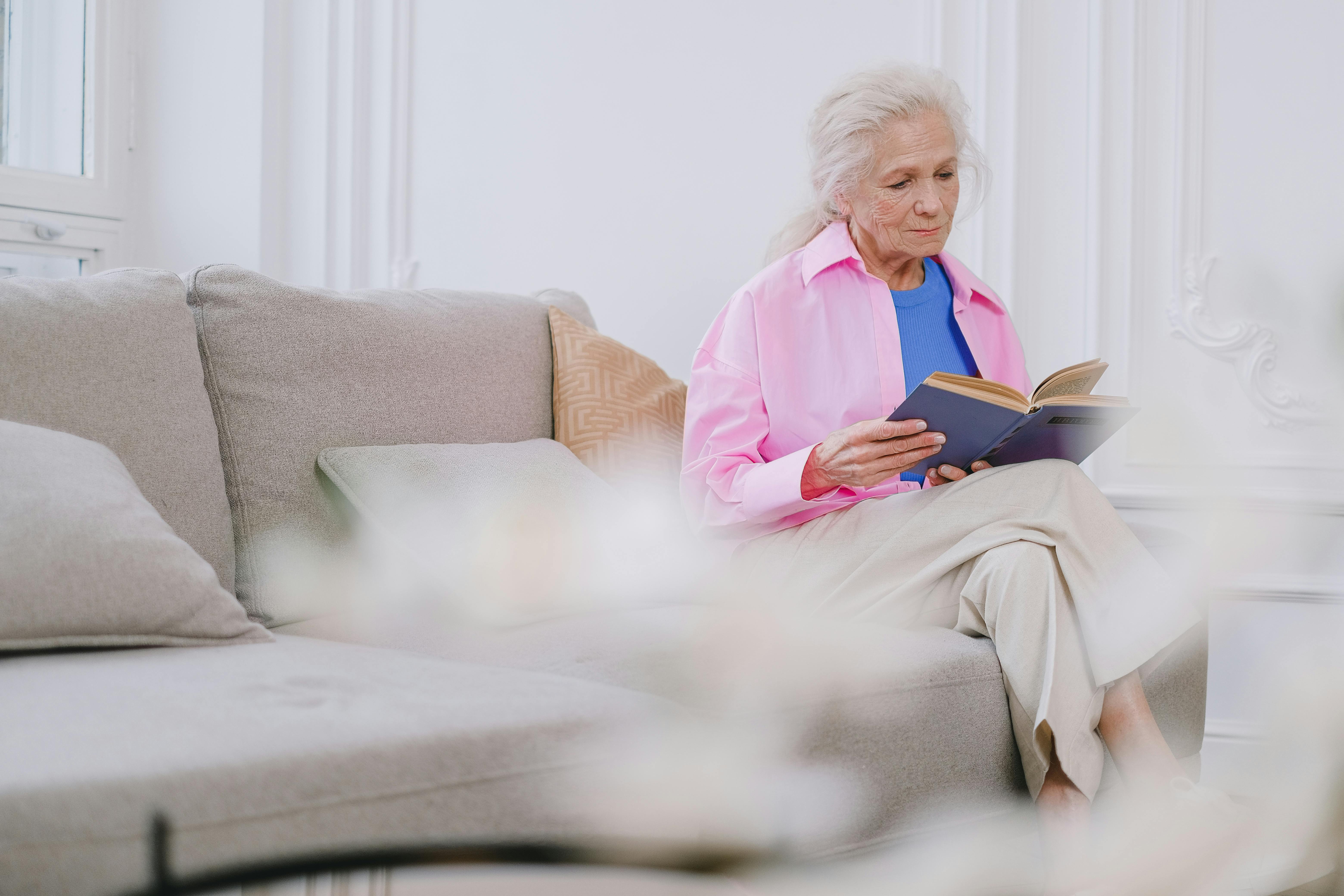 Senior woman enjoying a book while sitting on a sofa in a cozy and bright interior.