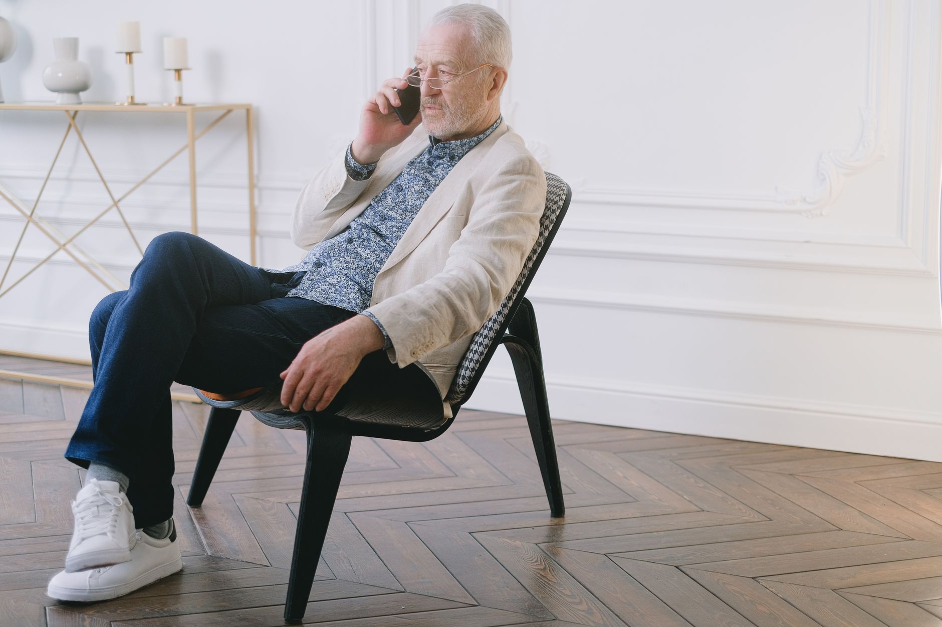 경기도 어르신 스마트폰 무료 교육 7 A senior man in stylish casual attire sitting on a chair indoors, using a smartphone.