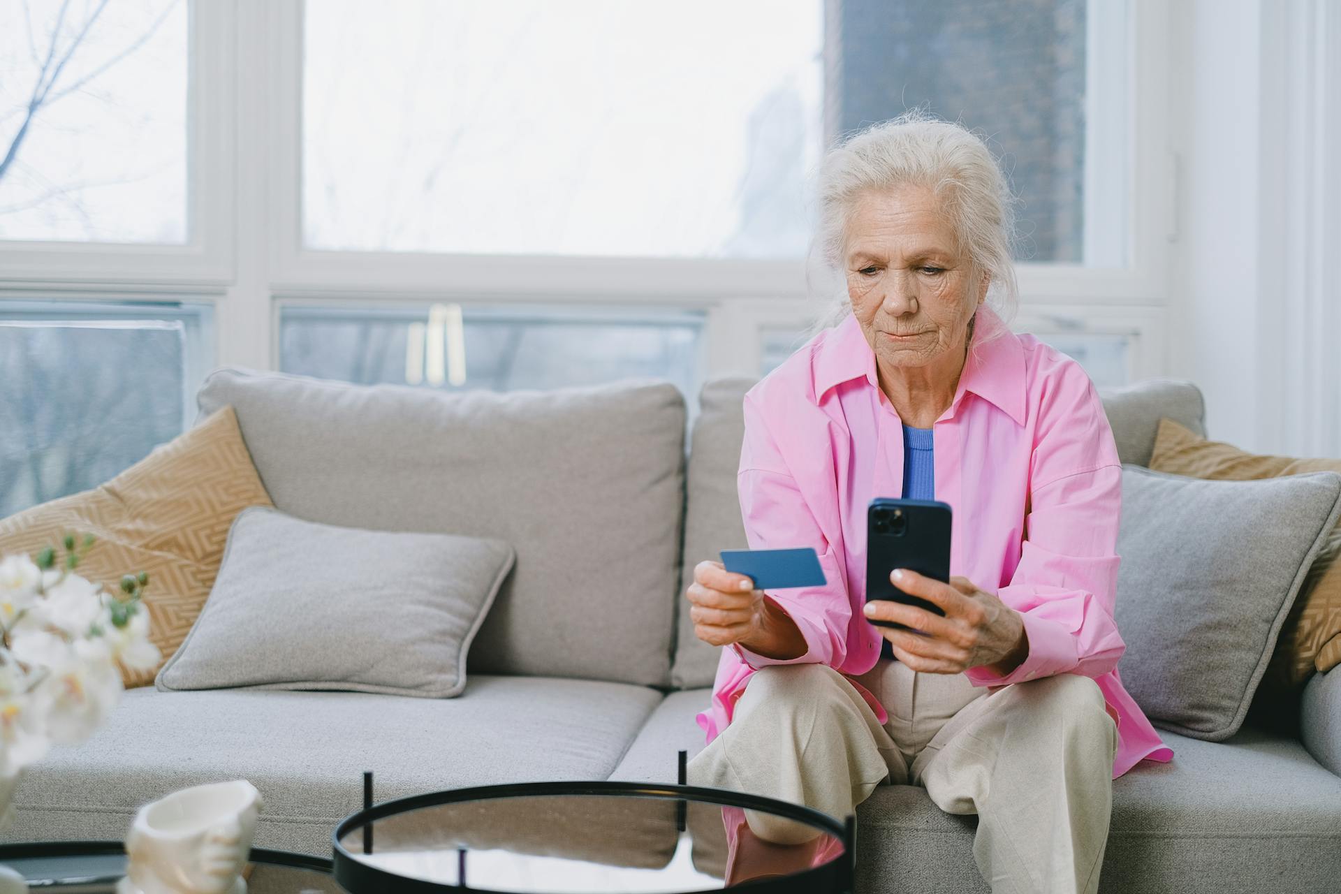 Elderly woman shopping online using smartphone and credit card indoors.