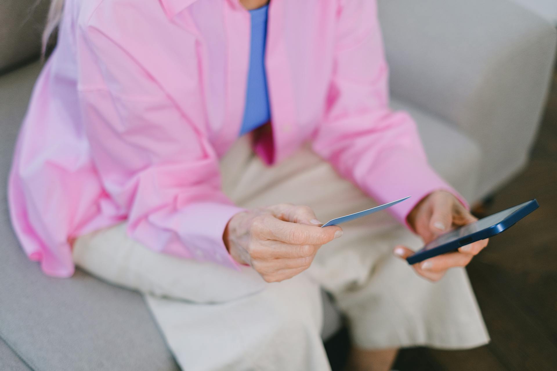 Elderly woman holds credit card and smartphone for online shopping.